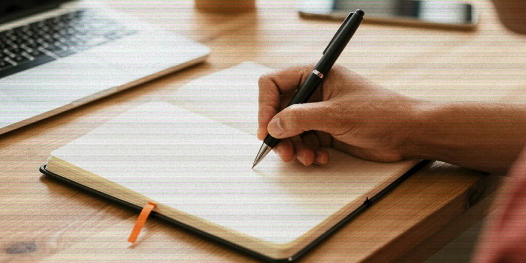 Pessoa escrevendo uma linha no caderno — próximo passo mínimo contra a procrastinação